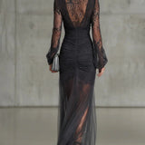 Vestido longo em renda cinza escuro, com babados, transparente, com mangas longas e fenda lateral.
